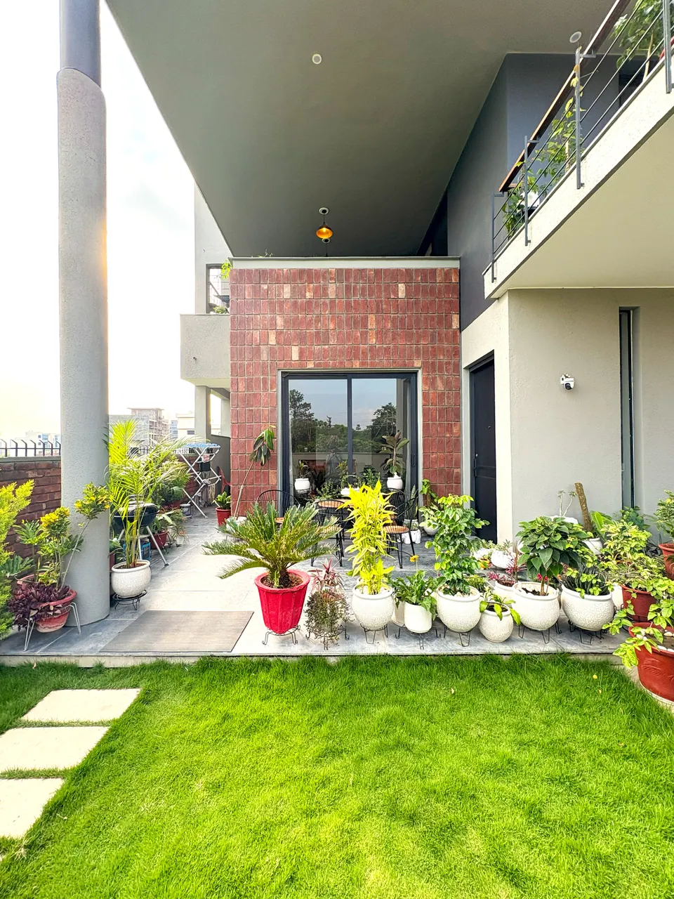 Garden front: a lawn and potted plants before the brick-clad block, with the cantilevered roof and a balcony above