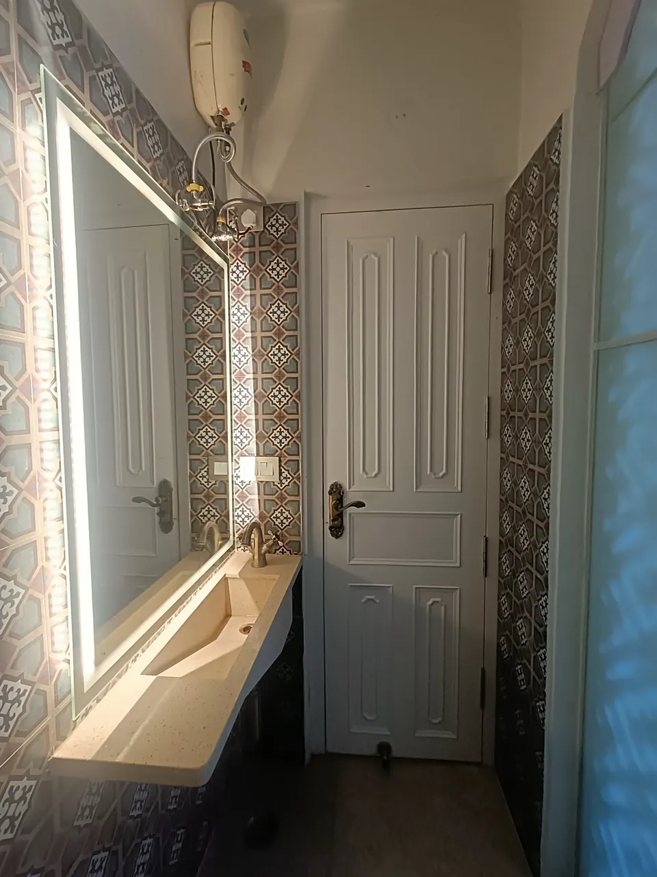 Powder room: patterned cement tiles, an illuminated mirror over a stone trough basin and a panelled white door