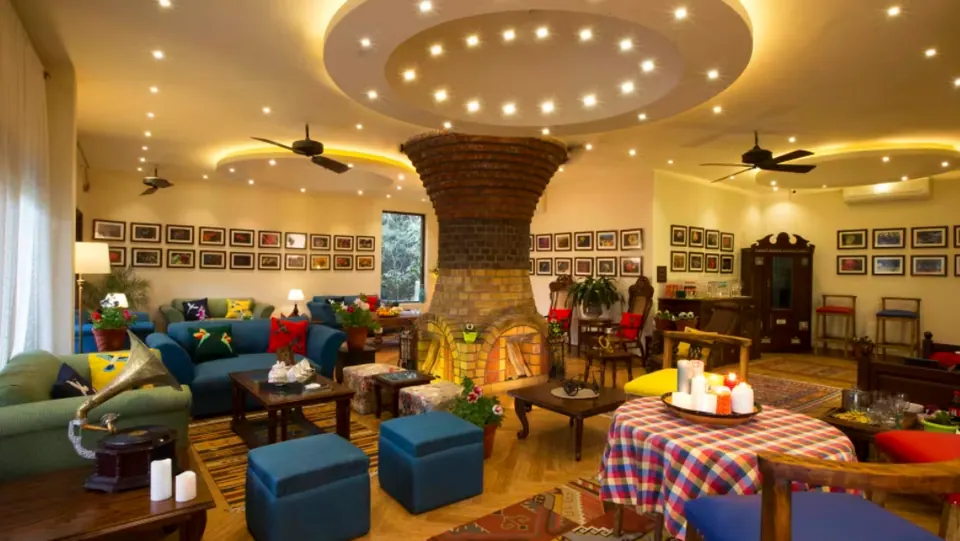Living room around an hourglass-shaped brick chimney: blue sofas, ottomans, a checked tablecloth and framed photographs