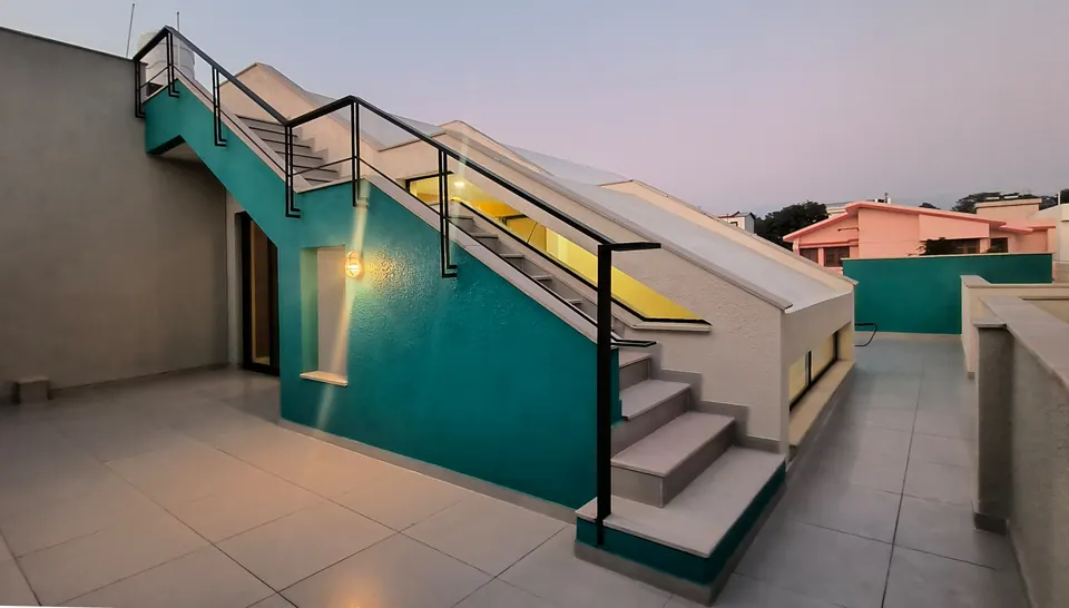 Roof terrace at dusk: an external stair along a teal wall with a black railing, a glowing skylight strip and a tiled floor