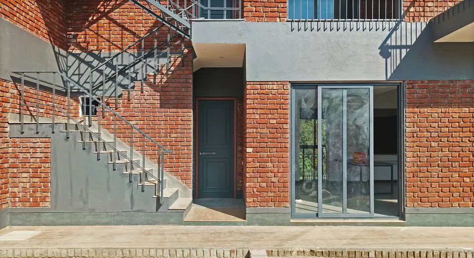 Ground floor: steel stair against brick and grey render beside a dark entrance door and a glazed sliding door