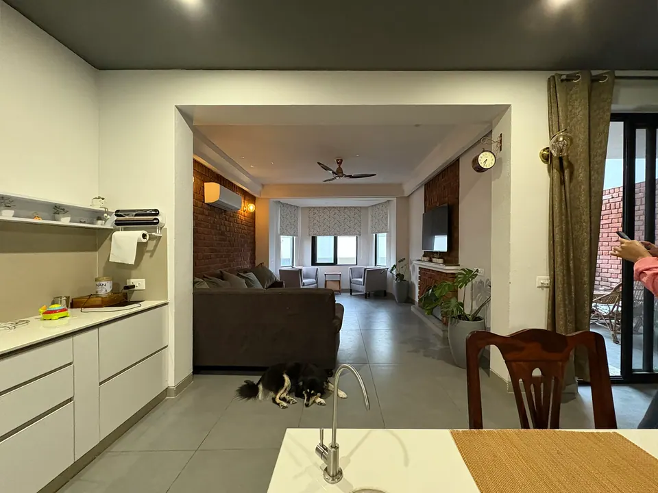 Kitchen counter in the foreground, a long living space with a sofa, a brick wall and a bay window, a dog on the floor