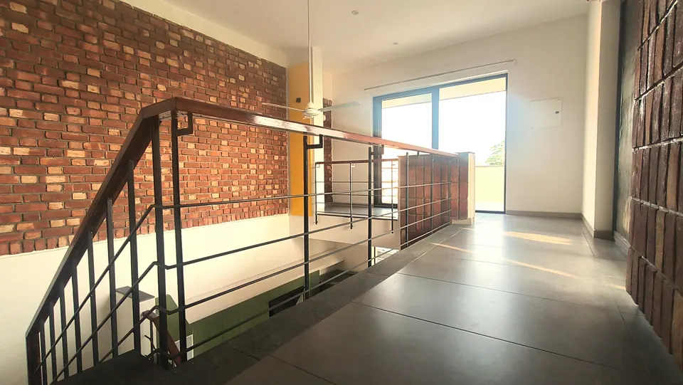 Upper landing with a brick wall, the stair balustrade and a glazed door to a terrace, sunlight on grey floor tiles