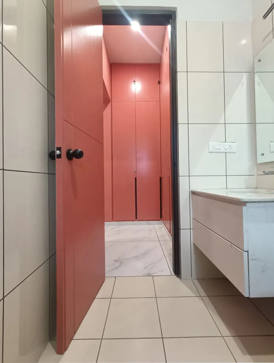 Bathroom with a coral door open to a coral-red walk-in wardrobe, white tiles and a wall-hung vanity