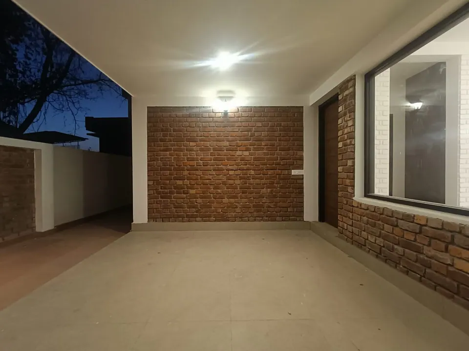 Covered porch at dusk: an exposed-brick wall, a black-framed window and a ceiling light over a pale floor