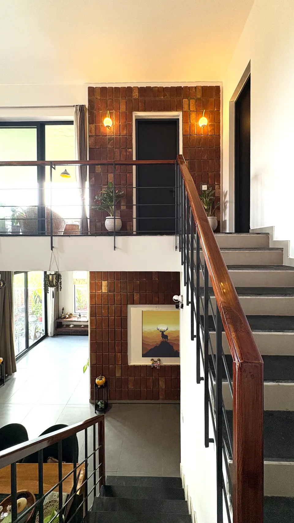 View down the stair from the upper landing into the dining area, a brick-tile wall with lights and a doorway
