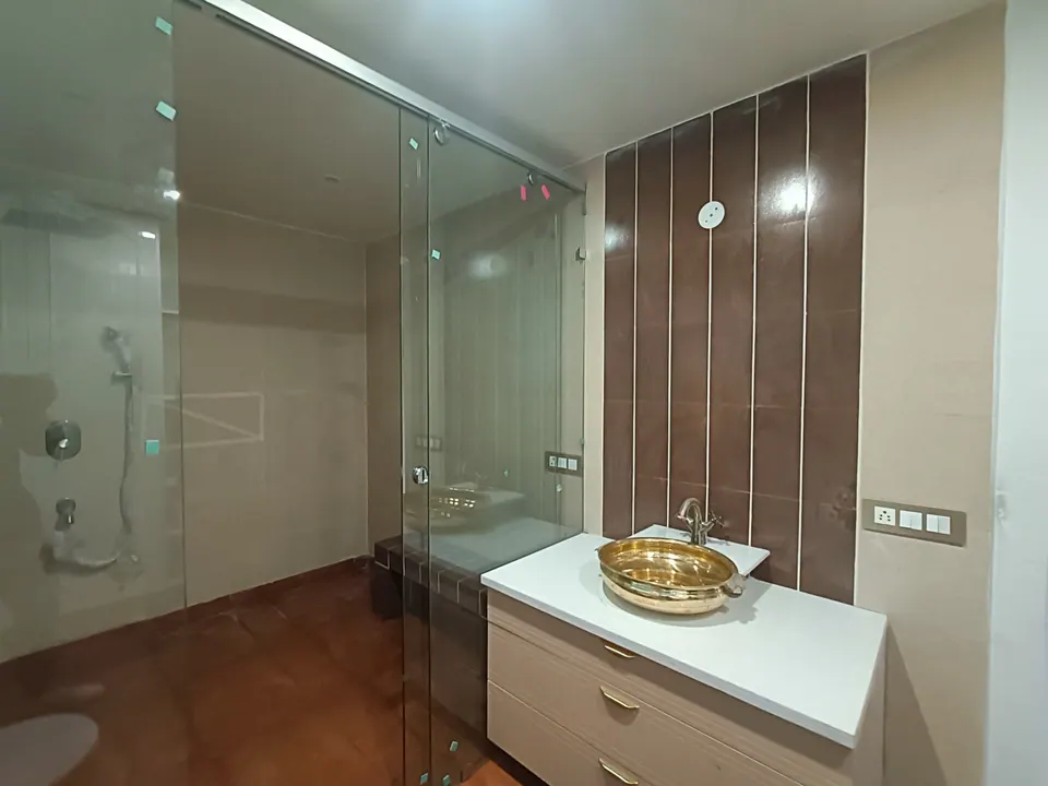 Bathroom with a brass vessel basin on a white vanity, a glass shower enclosure and a brown tiled wall