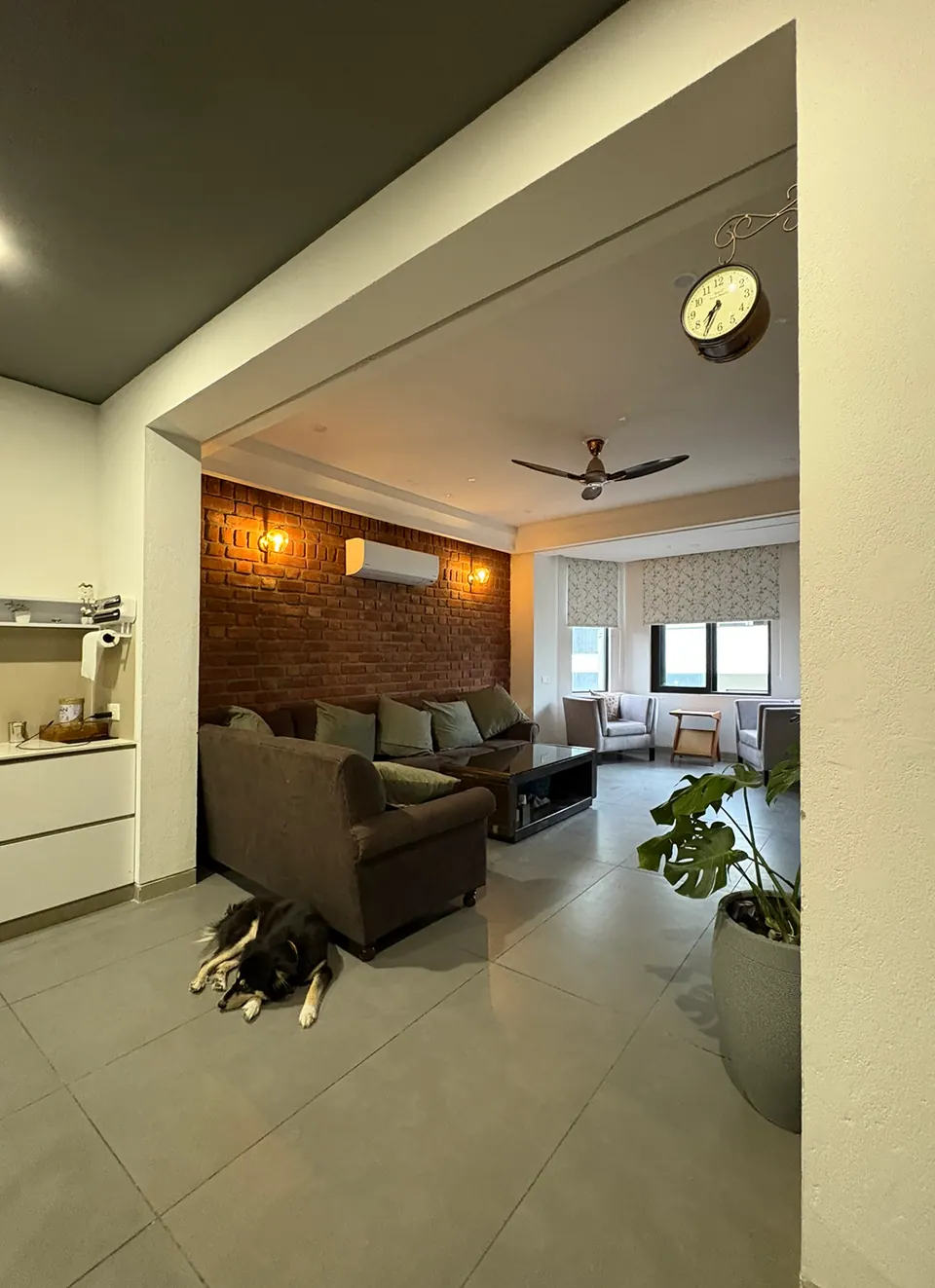 Living area through a wide opening: a sofa against a brick wall, a dog asleep on the floor and a bay window beyond