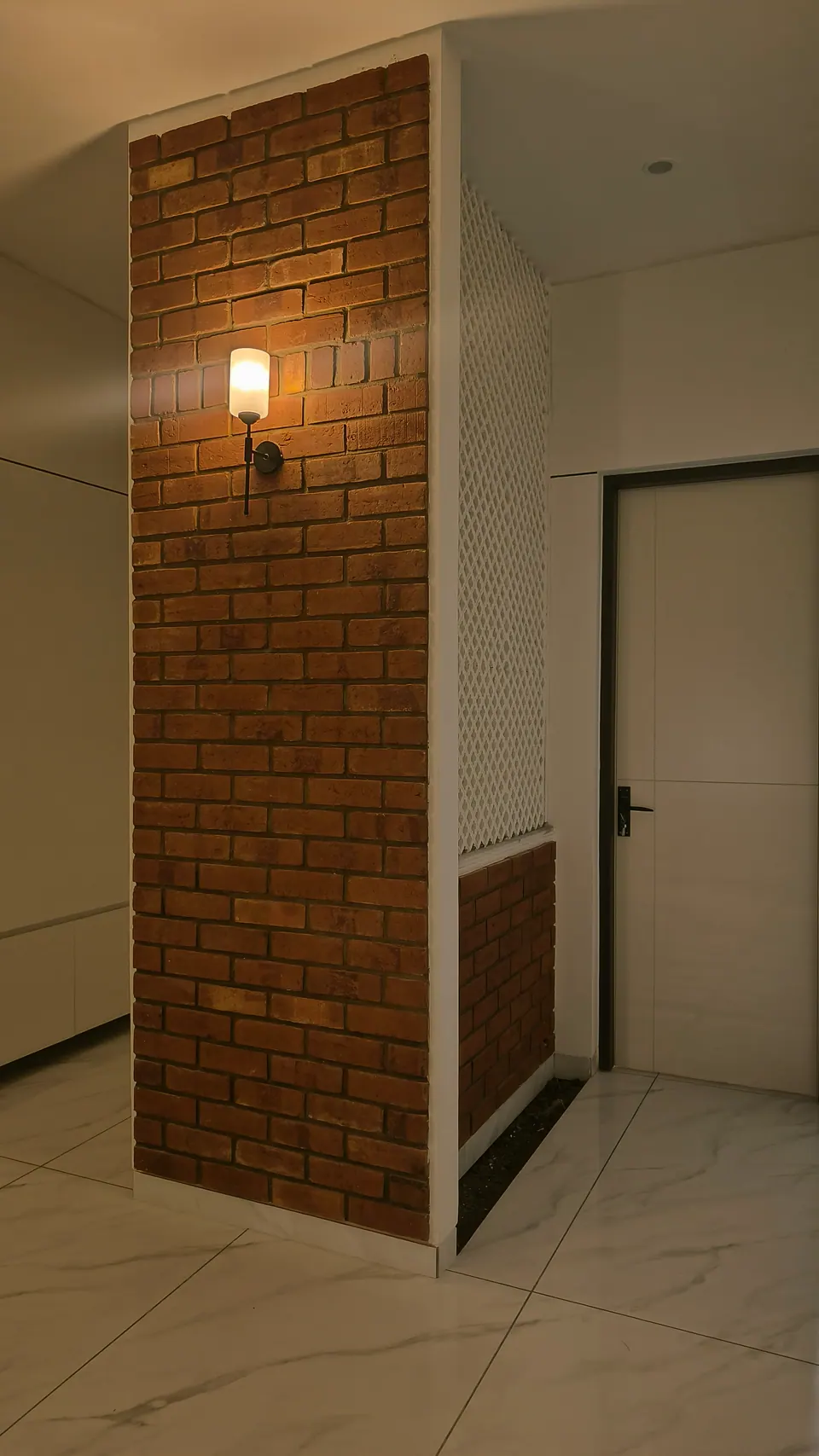 Exposed-brick wall with a wall lamp beside a white door and a white lattice screen