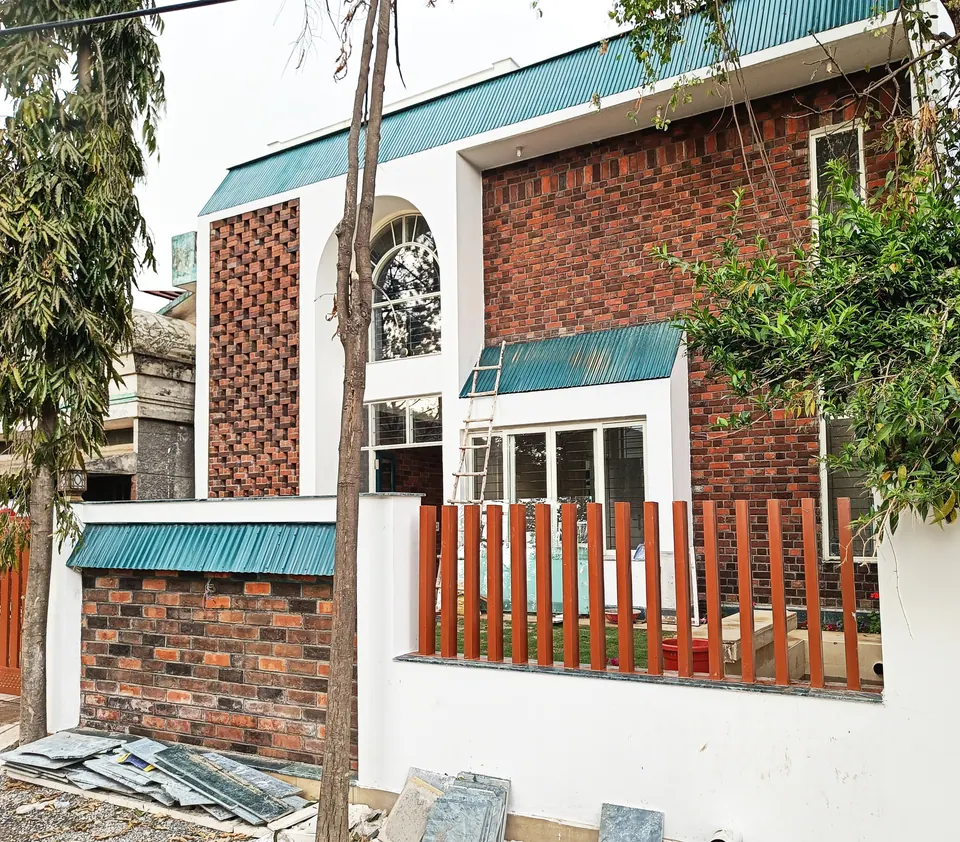 Corner of the front: exposed brick, an arched window, turquoise canopies and red slatted fencing behind two slender trees