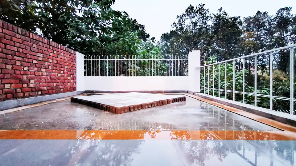 Wet paved terrace at dusk reflecting the trees, with a white parapet, railings and a brick boundary wall