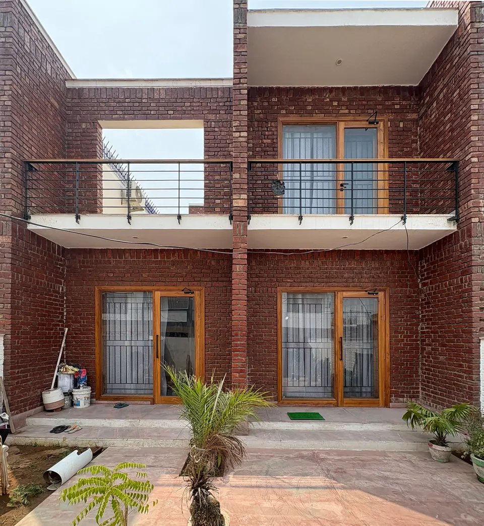 Front facade in exposed red brick: two cantilevered balconies with black steel railings over timber-framed glazed doors