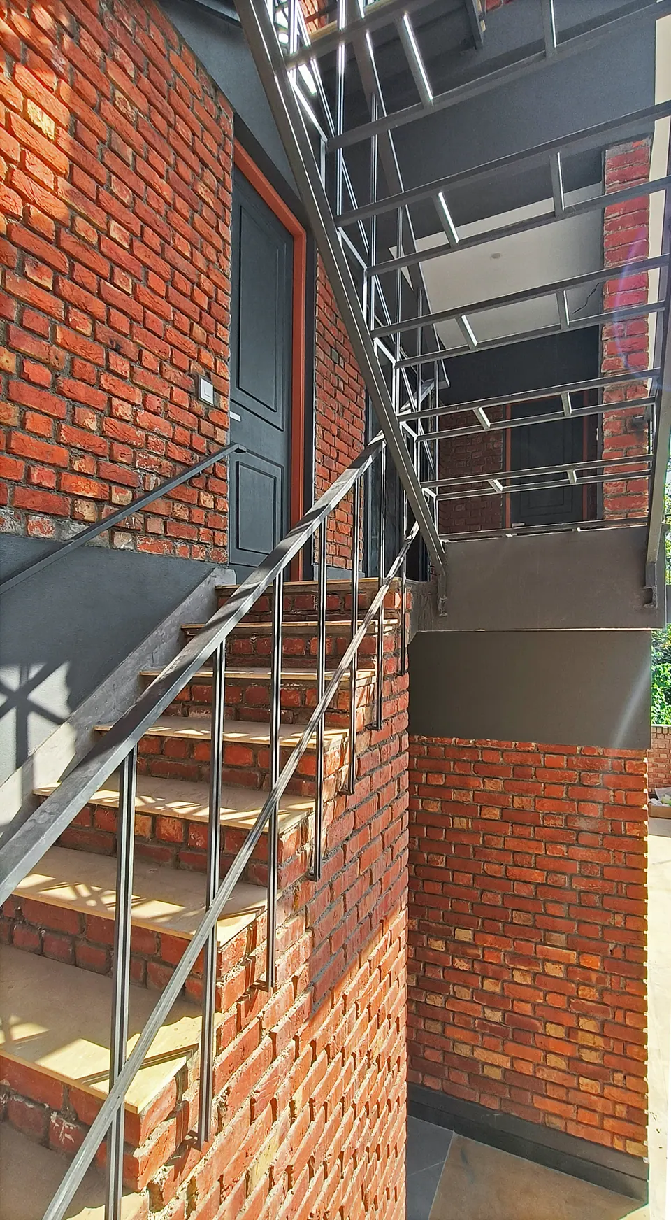 Steel stair with slender railings rising along a brick wall to an upper-floor door
