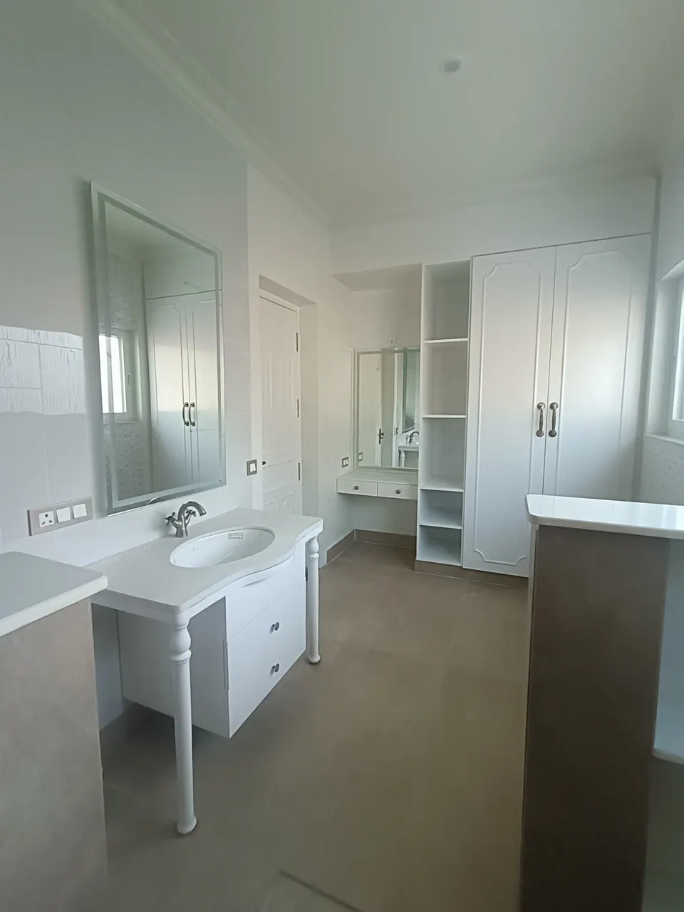 Bathroom with a white turned-leg vanity, a large mirror and white built-in wardrobes beside a dressing table