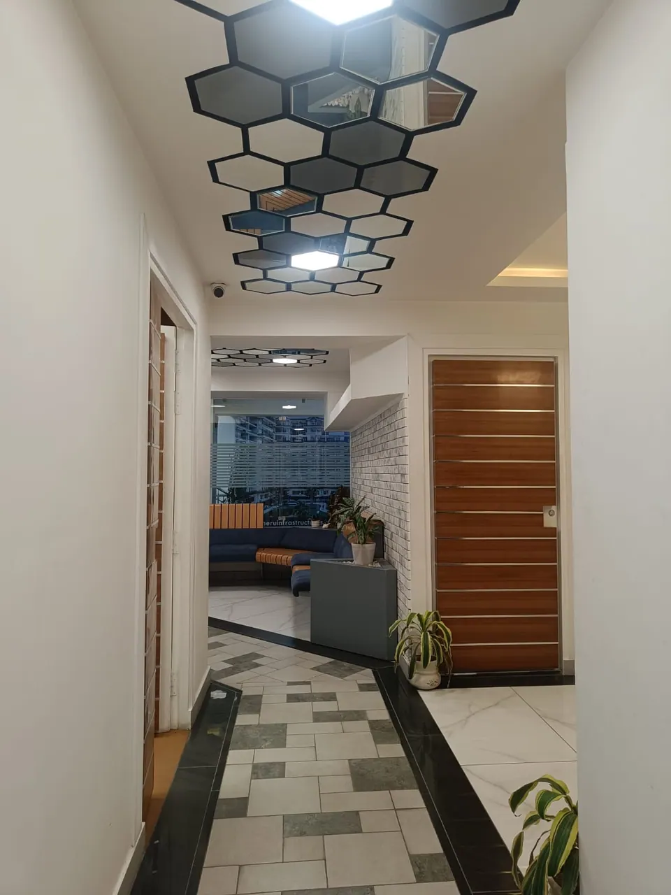 Corridor under hexagonal ceiling panels with a timber-striped door, opening to the lounge and its curved blue sofa