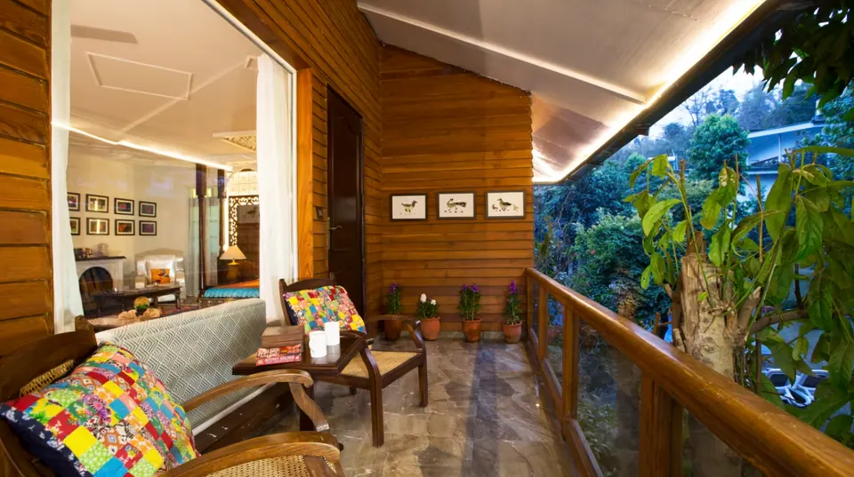 Timber-clad verandah with cane chairs and patchwork cushions, potted plants and a glass railing open to the trees
