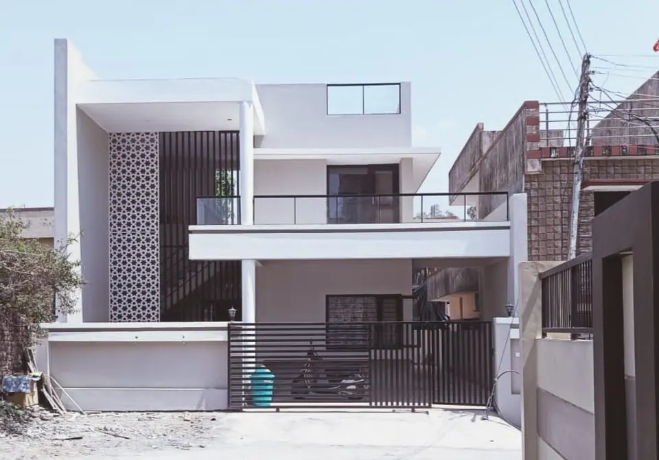 Two-storey white house with a patterned jaali screen, black vertical slats, a cantilevered frame and a glass-railed terrace