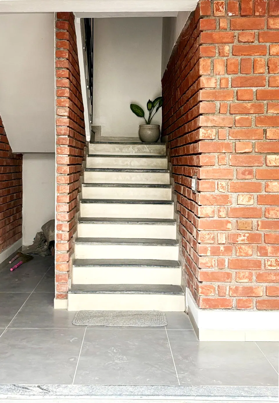 Stair between exposed-brick walls rising to a landing with a potted plant