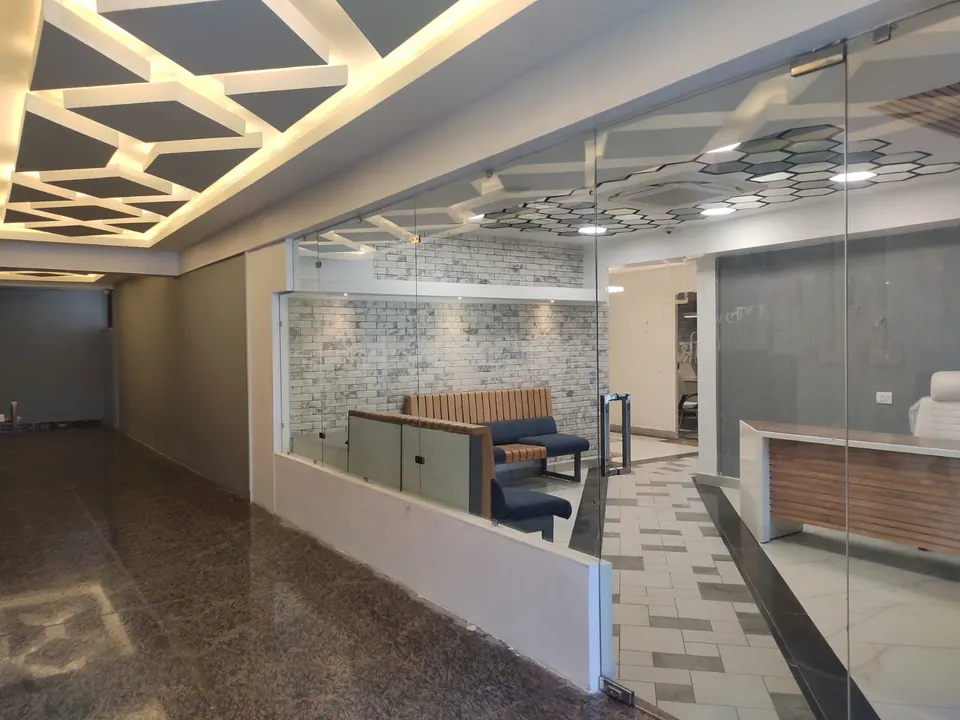Glass partition into the reception lounge, with a brick-effect wall, a blue sofa, a slatted counter and a lit ceiling grid
