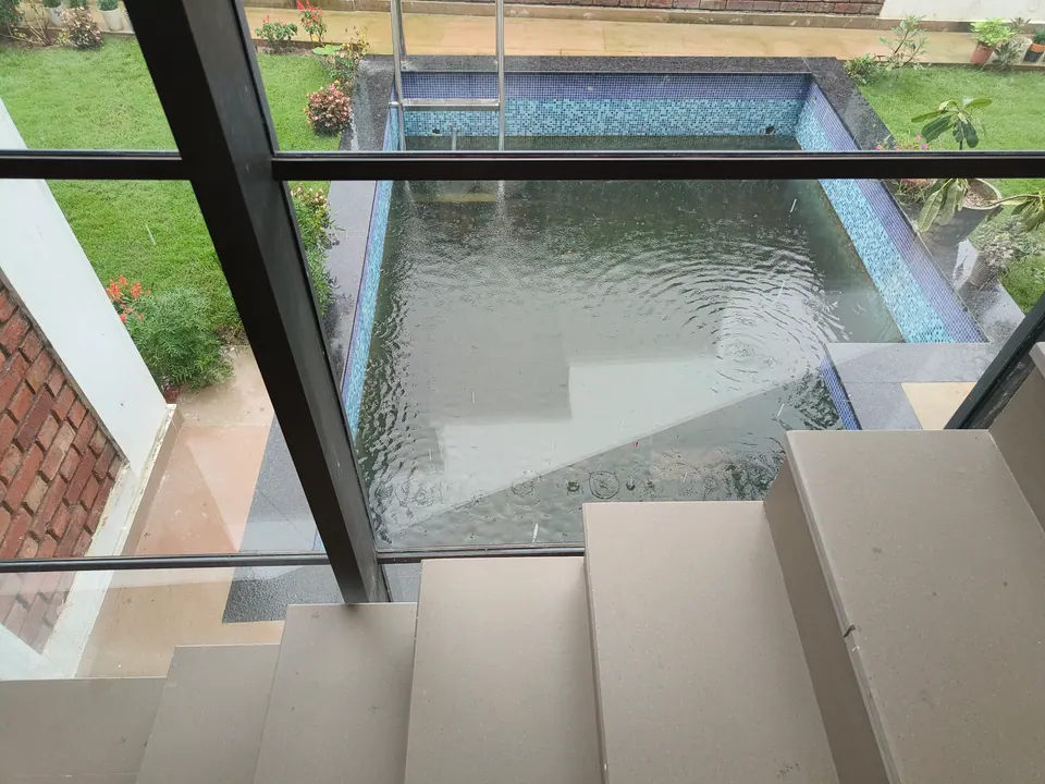 View down through glazing past concrete steps to the pool with a mosaic edge and a lawn