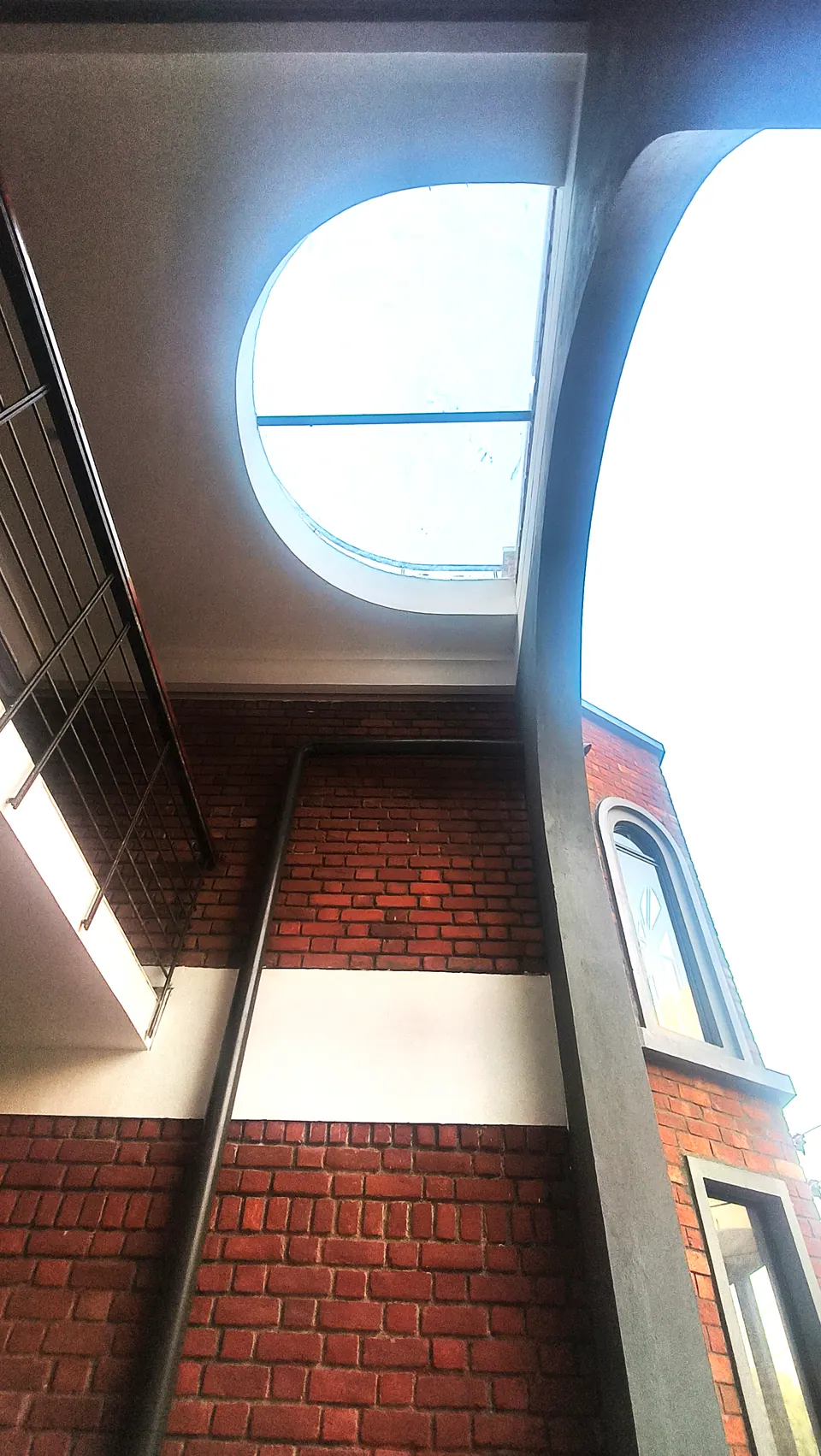 Looking up past the tall grey arch to an oval opening in the slab, brick walls and a bay window