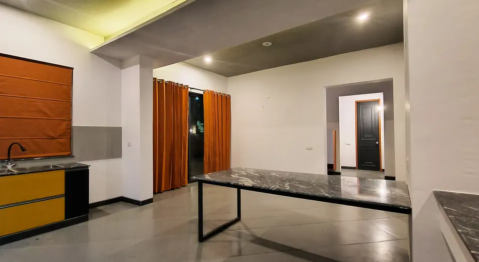 Kitchen and dining with yellow cabinets, a stone-topped table on a black steel frame and orange curtains