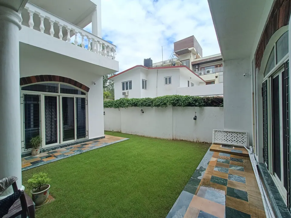 Courtyard lawn edged by a multicoloured stone path, with a white column and a balustraded balcony above