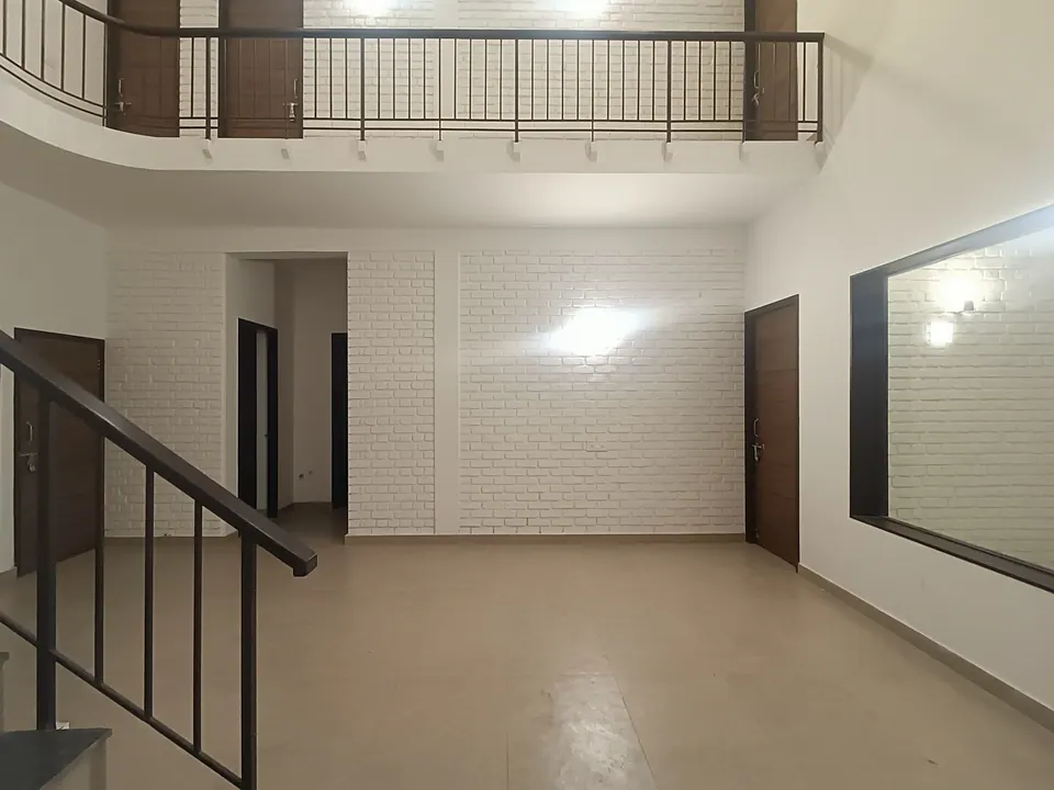 Double-height hall with white-painted brick walls, a stair with a black railing, an upper gallery and timber doors