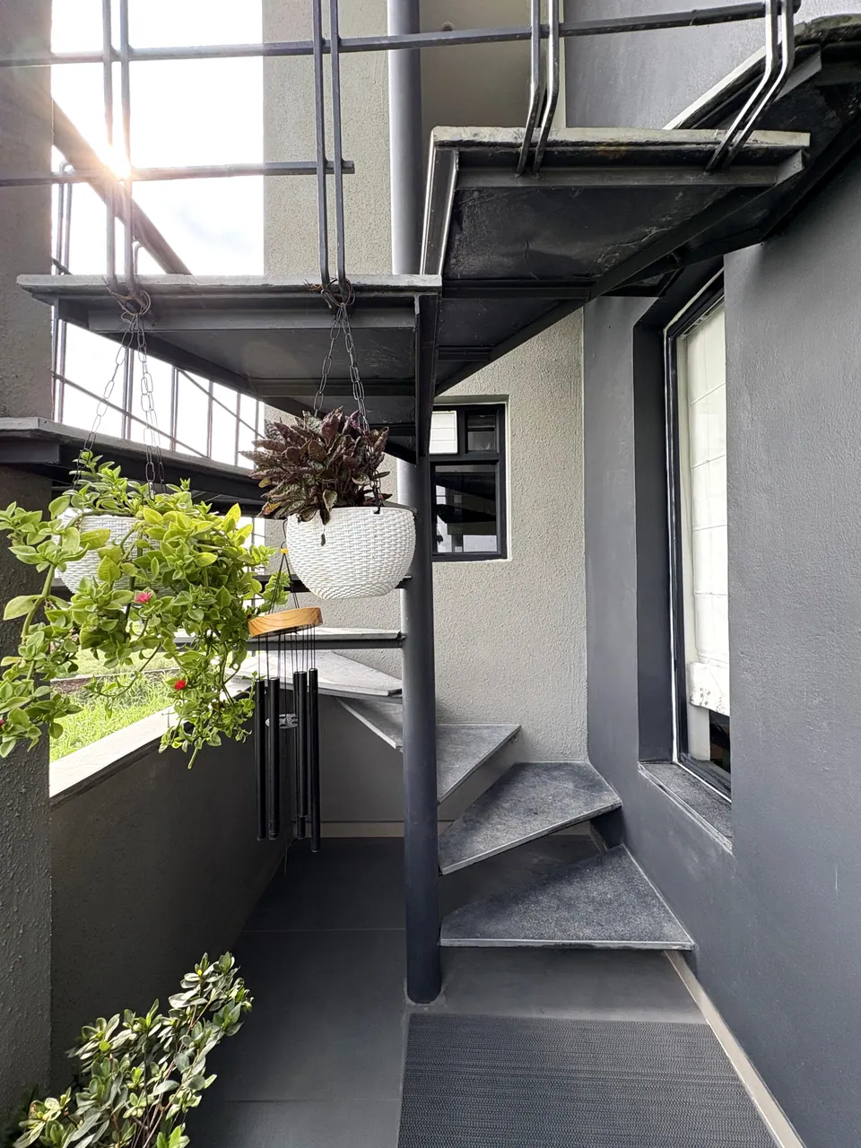 Steel spiral stair with grey treads on a balcony, hanging planters and wind chimes