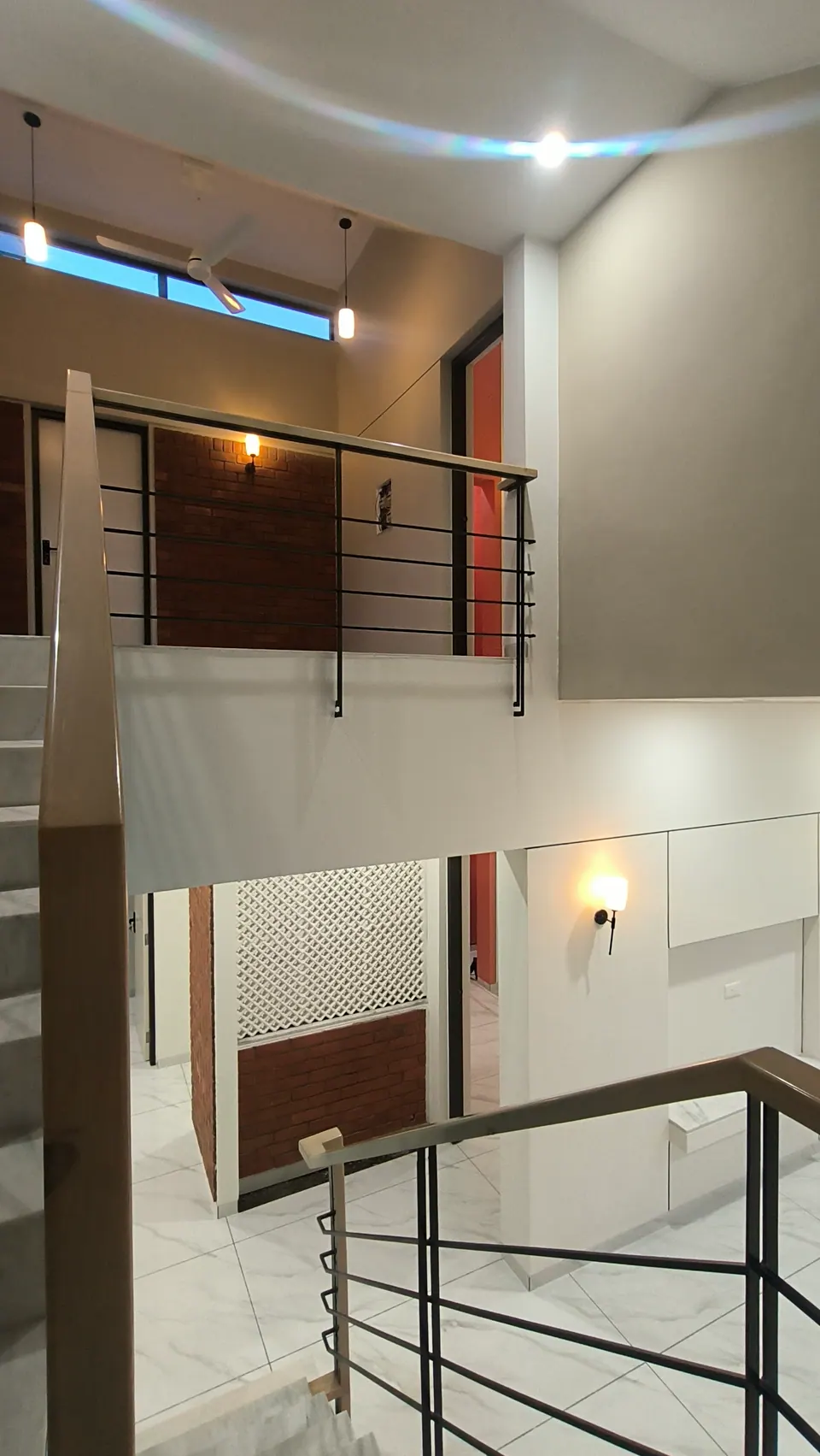 Upper landing overlooking the stair: a railing, a brick wall, a lattice screen and clerestory windows