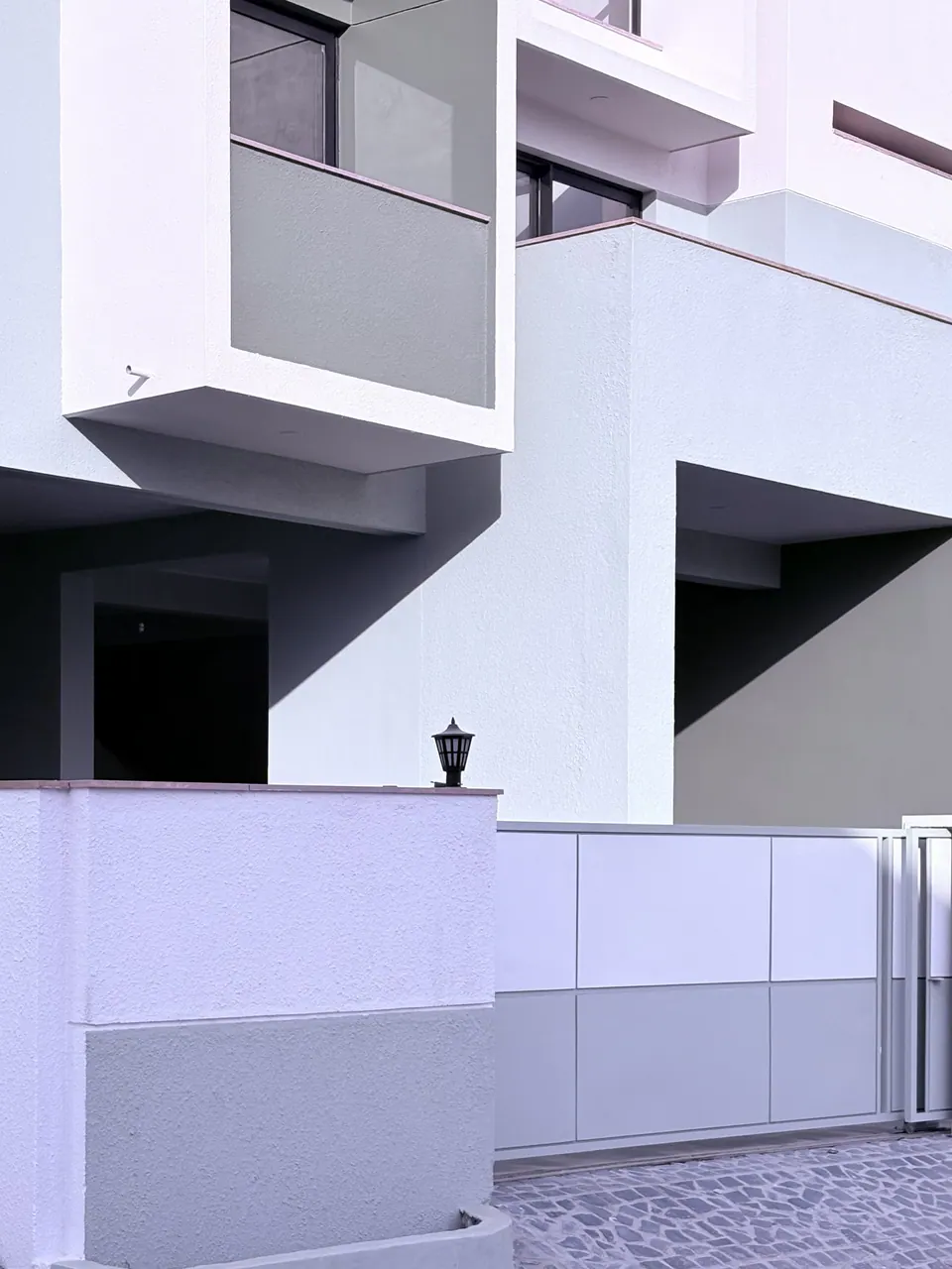 Projecting sage balcony box and white walls above the boundary wall, with a lantern and a sliding gate