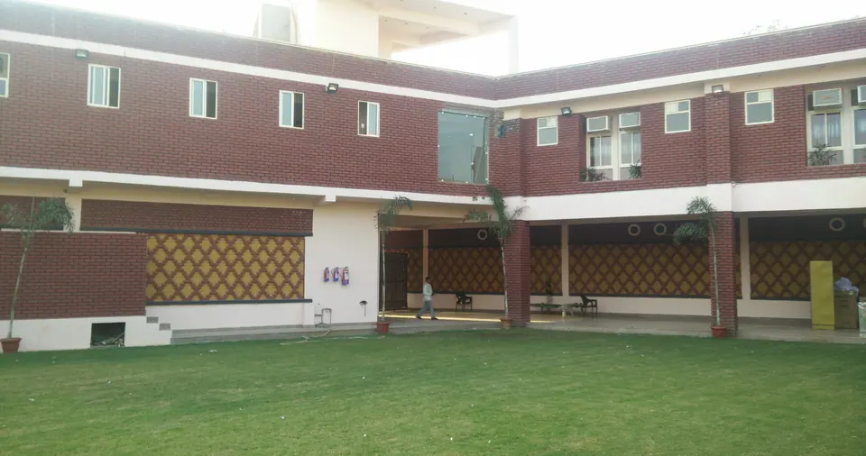 Inner lawn framed by the two-storey building: brick upper floor, white colonnade and red-and-yellow patterned brick panels