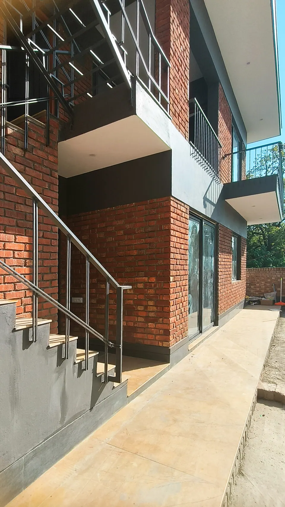 Steel stair with slender railings climbing the brick facade beneath a projecting balcony