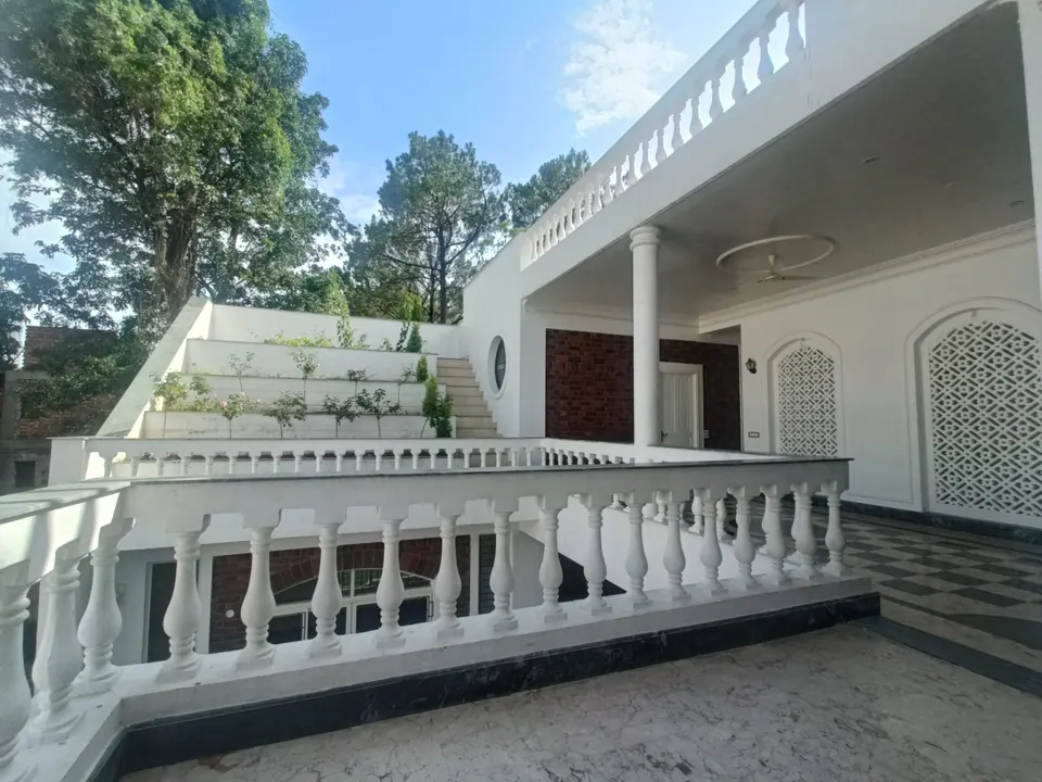 Upper verandah with a white balustrade, white jali panels and stepped planted terraces beyond, under pine trees