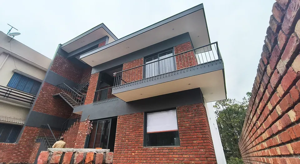 Brick house with grey bands, a cantilevered balcony and external steel stair, seen at a steep angle beside a brick wall