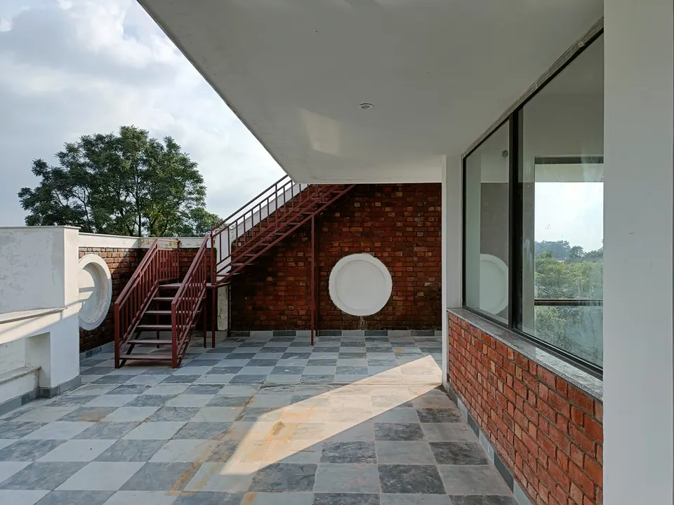 Covered terrace with a chequered stone floor, a brick wall with a round window and a red steel stair to the roof