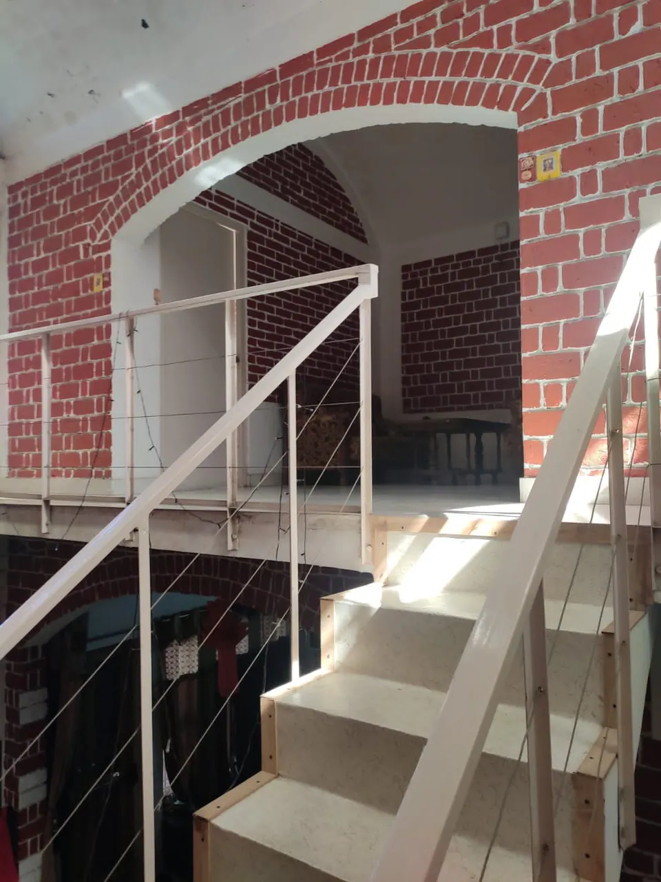 Stair and bridge with white steel railings beneath a red brick arch, above a lower level