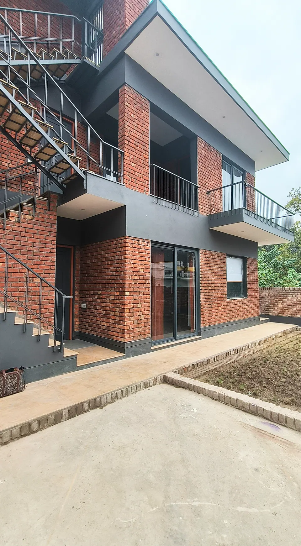 Brick facade with a grey band, an external steel stair to the upper floor and a deep roof overhang above a paved walk