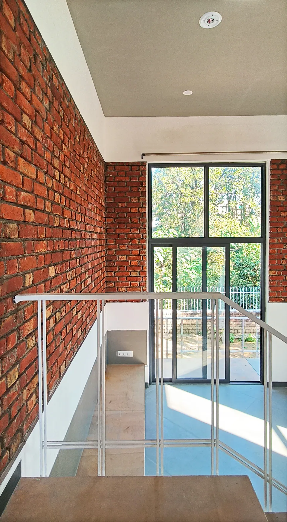 Double-height stair landing with an exposed brick wall and a tall window onto trees