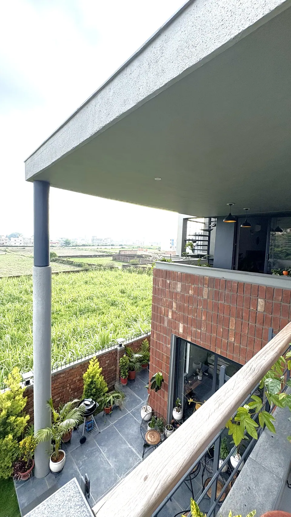 Balcony view along the cantilevered roof to the patio below, the brick-clad block and fields in the distance