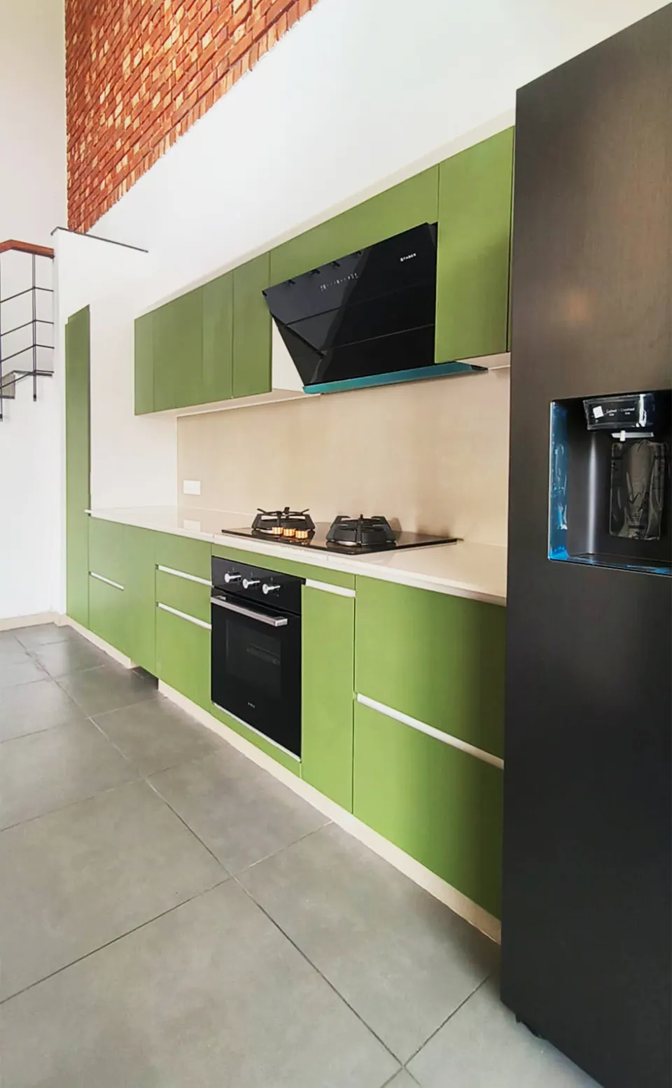 Kitchen with green handleless cabinets, a black chimney hood and a built-in oven, a dark fridge in the foreground