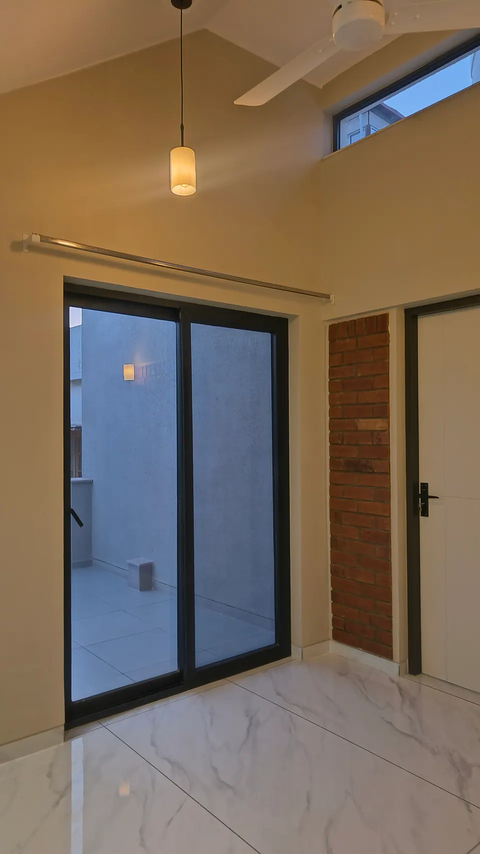 Room under a sloping ceiling with a black-framed sliding door to a terrace and an exposed-brick panel