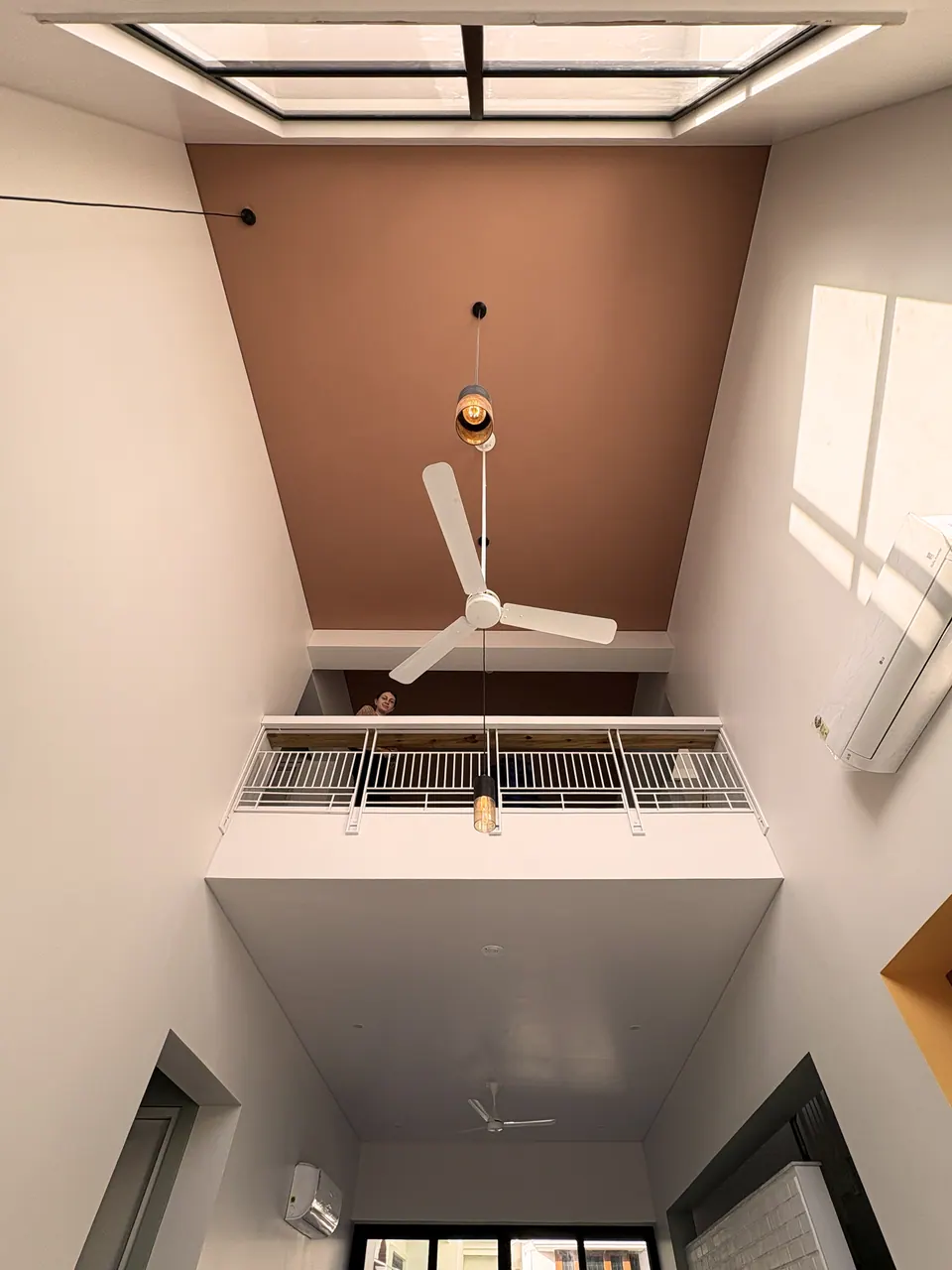 View up a double-height space to a skylight, a terracotta ceiling panel, a ceiling fan and a white-railed gallery