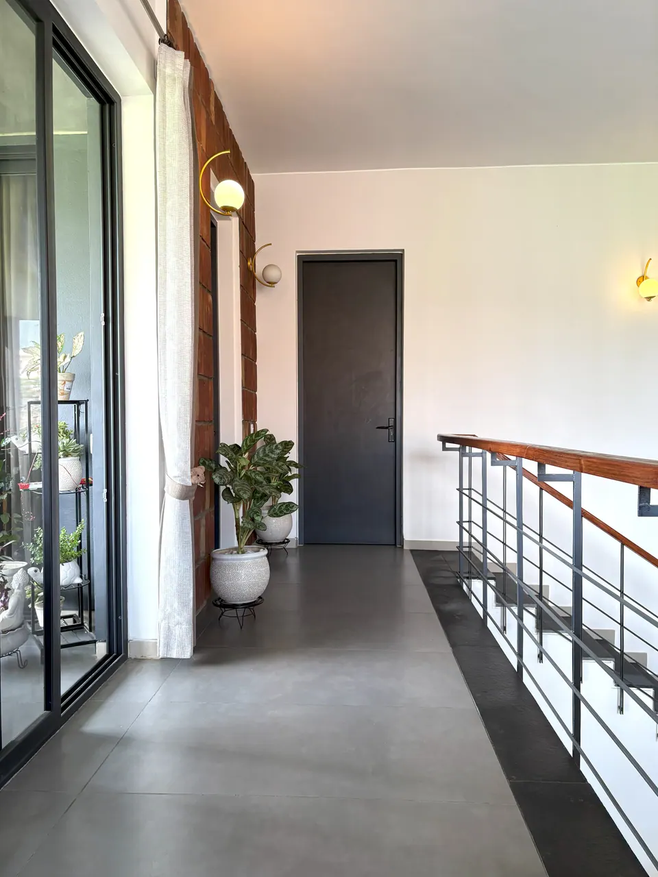 Upper corridor with a glazed door to a balcony, a dark door at the end and a railing along the stair void