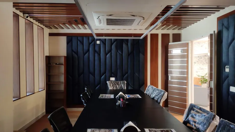 Conference room: a long black table and chairs before a wall of padded navy panels, under a timber-slatted ceiling