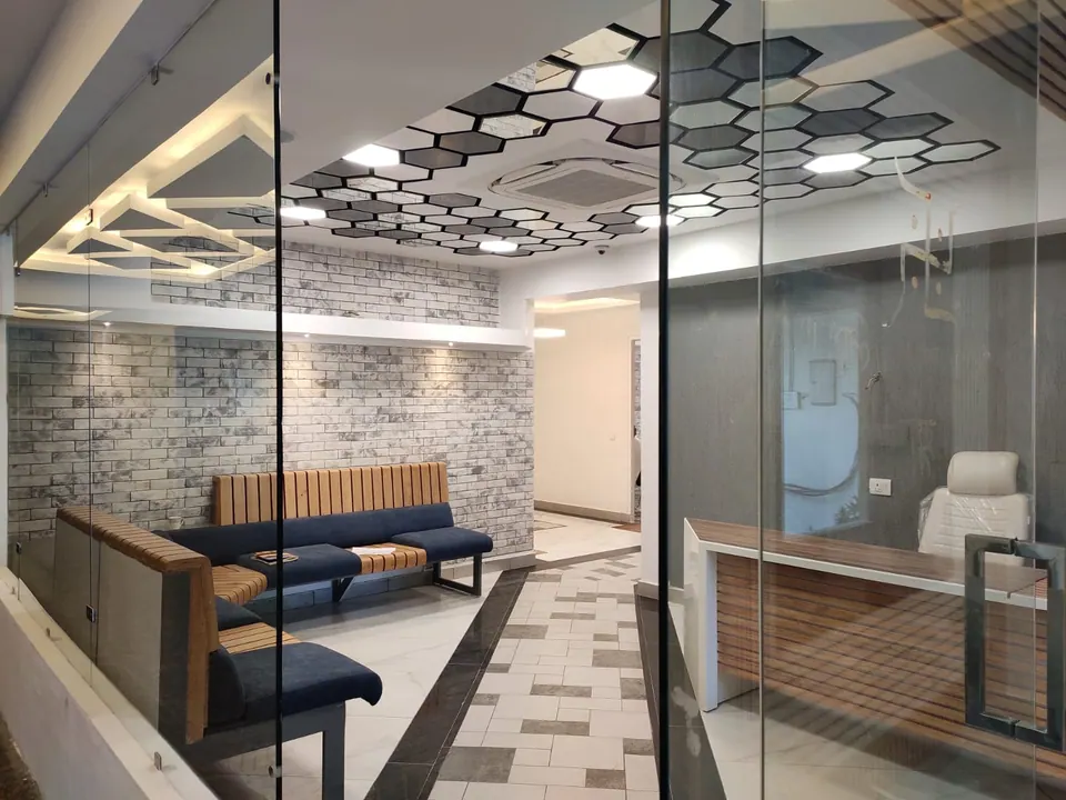 Reception lounge behind a glass partition: a curved blue sofa with timber slats, a brick-effect wall and a hexagonal ceiling