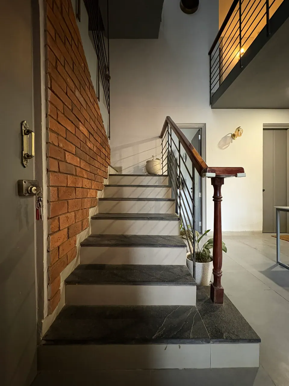 Stair with dark stone treads along an exposed-brick wall, a timber newel post and black steel balusters