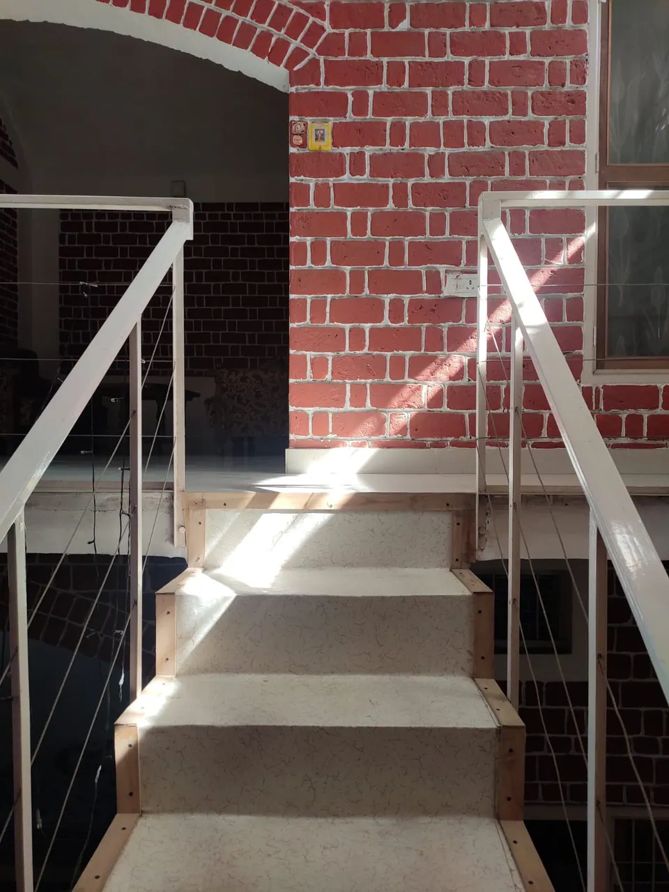 Stair with terrazzo treads and white steel railings rising towards a red brick wall with an arch