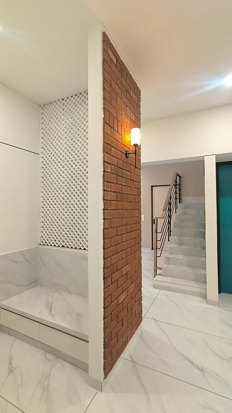 Brick pier with a wall lamp beside a white lattice screen, the marble stair beyond