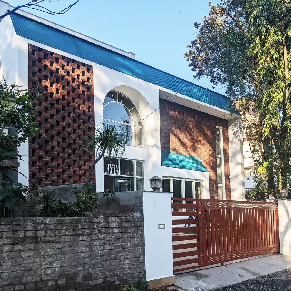 Street front: a white house with turquoise metal roofs, a brick jali panel, an arched window and a slatted red sliding gate